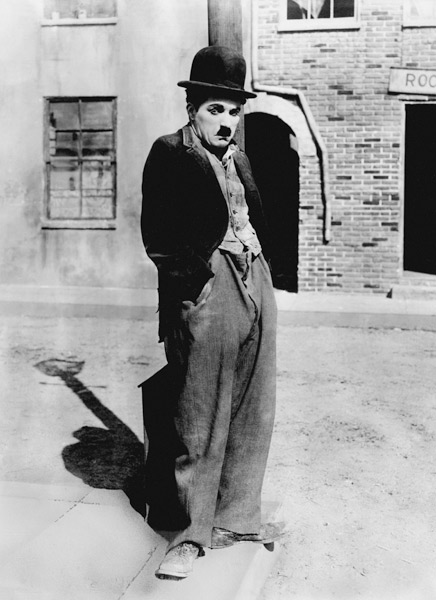A dog 's life by and with Charlie Chaplin , standing in a street, hands in pockets. Los Angeles de English Photographer, (20th century)