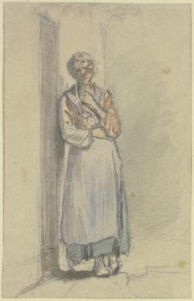 Eine Frau steht mit der rechten Schulter an die Haustür angelehnt, die linke Hand greift in das Deko